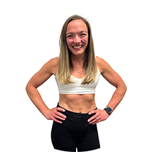 Smiling woman in a white sports bra and black leggings stands with hands on hips against a white background.