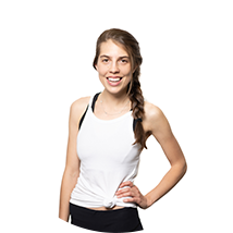 Smiling woman with long braided hair wearing a white tank top and black leggings, standing with one hand on her hip.