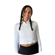 Smiling young woman with two braids wearing a white cropped long-sleeve top and black pants.