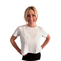 Smiling woman with hands on hips, wearing a white t-shirt and black pants, against a white background.